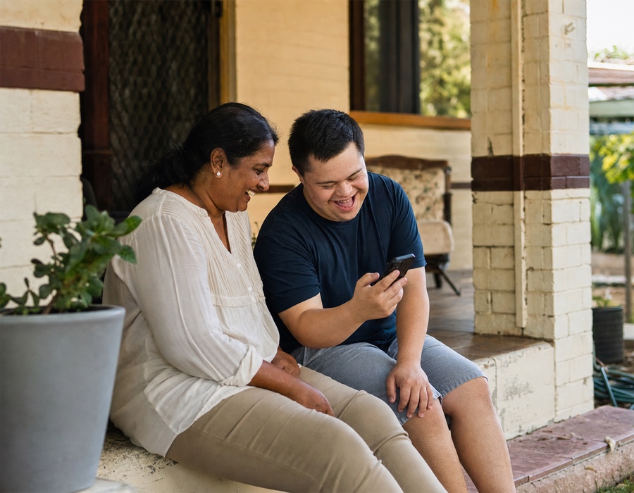 An adult participant and another person looking at a phone together on a front verandah