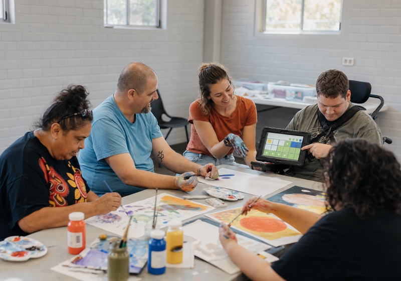 A group taking part in an art activity, with a support worker alongside a participant using a communication device